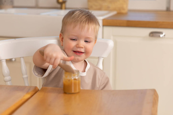 Щаслива родина вдома. Хлопчик годує себе на кухні. Маленький хлопчик з пухнастим смішним обличчям їсть здорову їжу. Дитина вчиться їсти сам тримаючи ложку. Самого годування
 - Фото, зображення