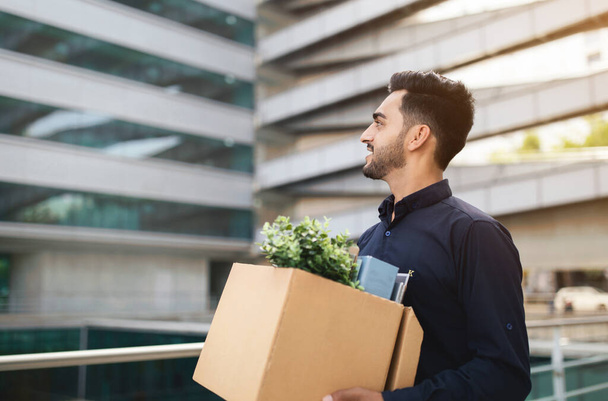 Empresário árabe homem com pertences caixa deixando centro de escritório contemporâneo com um sorriso. Desafios e oportunidades de emprego, início de um novo conceito de carreira. Espaço livre - Foto, Imagem