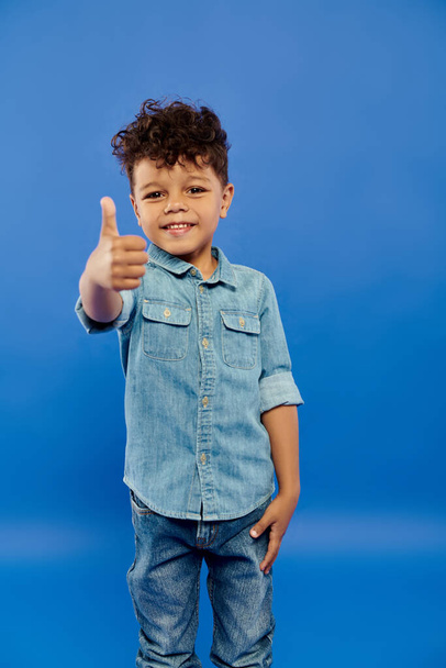 kręcone afrykański amerykański przedszkolak chłopiec w stylowy dżinsowy strój pokazując jak na niebieskim tle - Zdjęcie, obraz