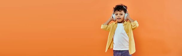 heureux et bouclé afro-américain garçon écouter de la musique dans des écouteurs sans fil sur orange, bannière - Photo, image