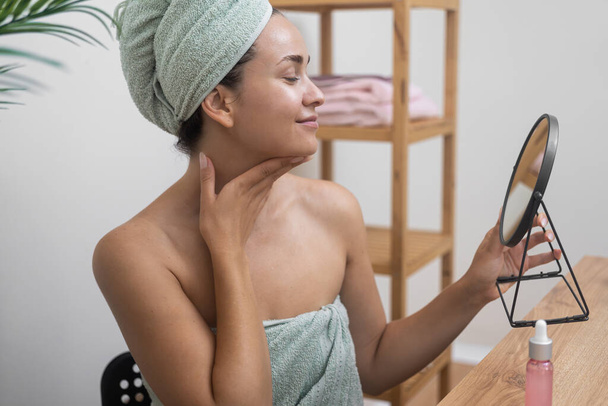 Kozmetikai rituálé: Egy nő az öltözőasztalánál megérinti ragyogó bőrét, miközben egy kerek tükörbe néz kozmetikai kényeztetés közben.  - Fotó, kép