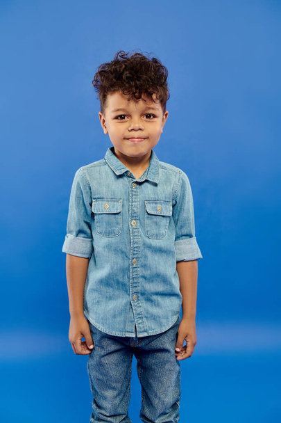portrait de heureux garçon afro-américain en costume de denim regardant la caméra sur fond bleu - Photo, image