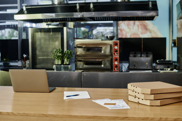 laptop κοντά σε κουτιά πίτσας και κάρτες μενού σε ξύλινο πάγκο σε μοντέρνο καφέ περιβάλλον, ζεστή ατμόσφαιρα - Φωτογραφία, εικόνα