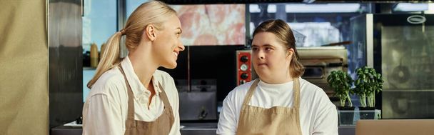 positive administrator talking to young female employee with down syndrome in modern cafe, banner - Photo, Image