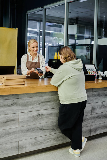 młoda klientka z zespołem Downa posiadająca kartę kredytową w pobliżu menedżera z terminalem w kawiarni - Zdjęcie, obraz