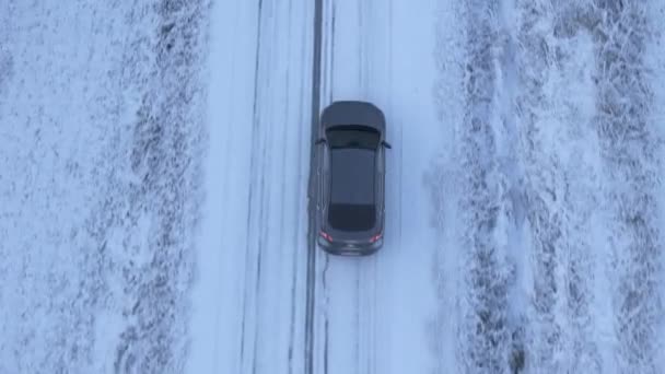 Luchtfoto van een elektrische auto die in de winter door de landweg rijdt met sneeuw op de ijzige weg. D-LOG-M kleurprofiel - Video