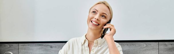 mujer rubia alegre sonriendo durante la conversación en el teléfono móvil en la cafetería, pancarta horizontal - Foto, imagen