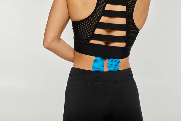 обрізаний вид молодої жінки в чорному спортивному одязі, позує кінезіологічними стрічками на спині - Фото, зображення