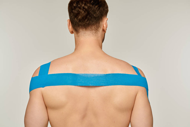 Rückenansicht eines athletischen männlichen Models, das mit kinesiologischen Bändern auf seinen Schultern und seinem Rücken posiert - Foto, Bild