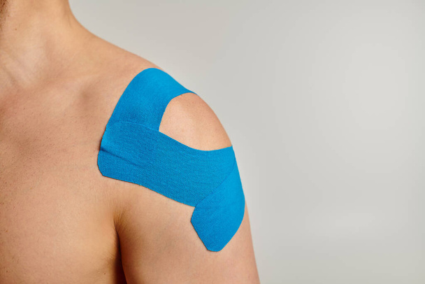 обрезанный вид человека с синими кинезиологическими лентами на плече, позирующего на сером фоне - Фото, изображение