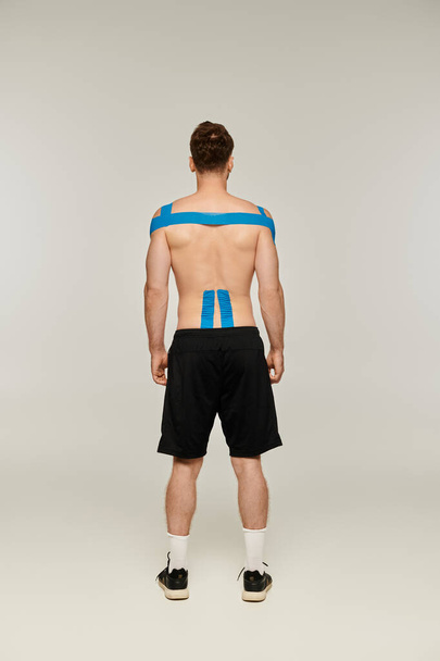 Вид сзади человека в черных спортивных штанах с кинезиологическими лентами на теле на спине - Фото, изображение