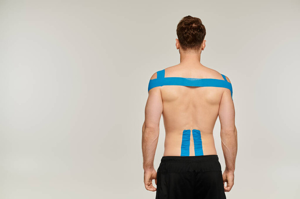 visszapillantás férfi sport nadrág kineziológiai szalagok a hát és a váll szürke háttér - Fotó, kép