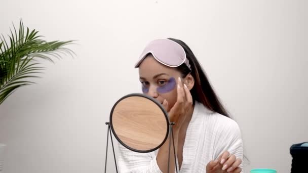 Ontwaken schoonheid: Een vrouw ochtend routine ontvouwt als ze pakt wallen, rimpels, en donkere kringen, staren in de spiegel terwijl het dragen van onder-oog maskers.  - Video