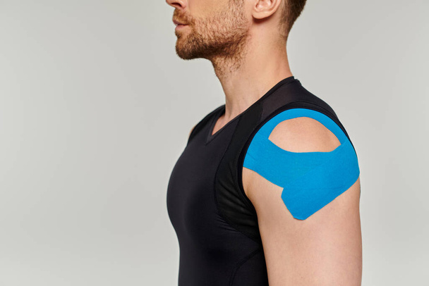Ausgeschnittene Ansicht eines bärtigen Mannes im schwarzen Sportoutfit mit kinesiologischen Klebebändern an der Schulter - Foto, Bild