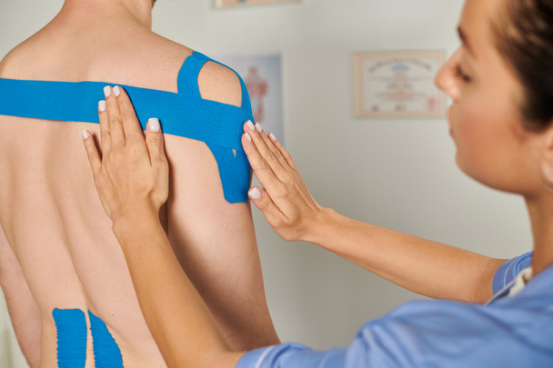 vue recadrée du jeune médecin féminin mettant des bandes kinésiologiques bleues sur sa patiente, soins de santé - Photo, image