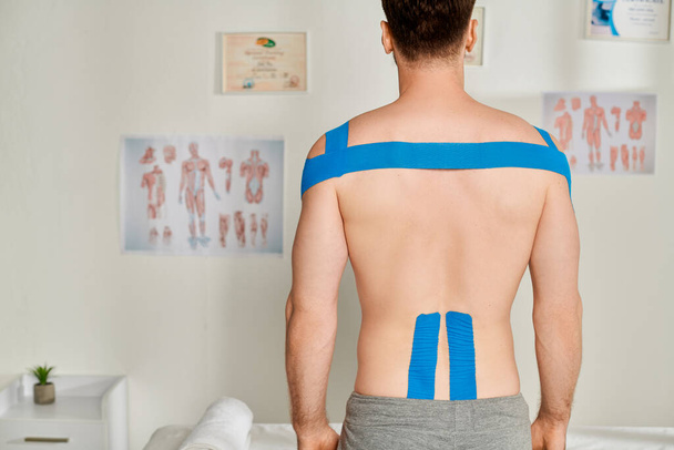 vue arrière du patient masculin pendant le rendez-vous avec des bandes kinésiologiques sur son dos et ses épaules - Photo, image