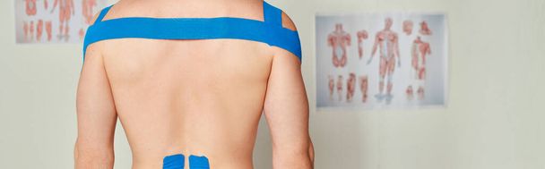visão cortada de paciente do sexo masculino em consultório médico com fitas kinesio em suas costas e ombros, bandeira - Foto, Imagem
