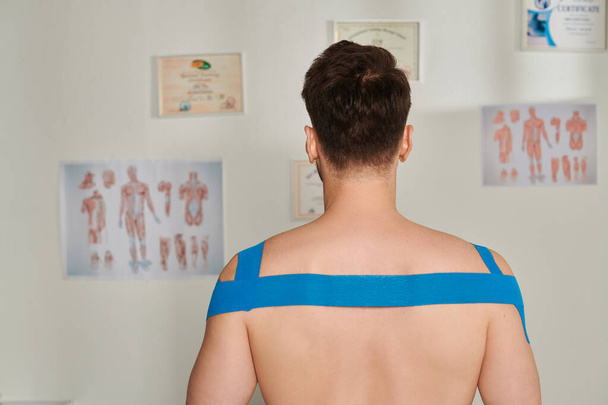 Rückenansicht des Mannes mit kinesiologischen Tapes an den Schultern und am Rücken während des Termins, Gesundheitswesen - Foto, Bild