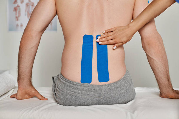 levágott kilátás fiatal orvos hátán a beteg kineziológiai szalagok, egészségügyi ellátás - Fotó, kép