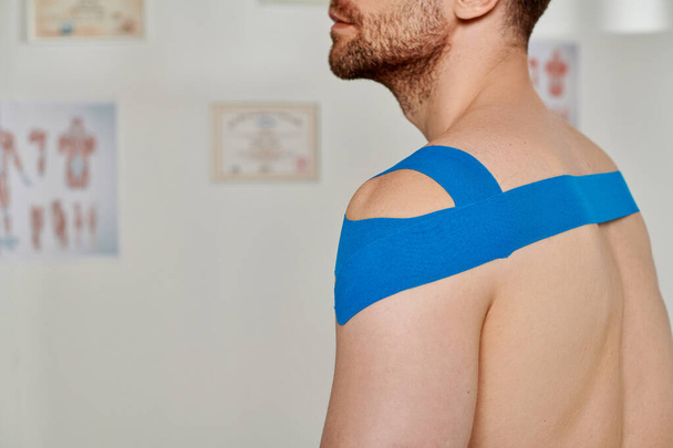 Ausgeschnittene Ansicht eines Mannes mit blauen kinesiologischen Bändern an der Schulter während eines Termins, Gesundheitsversorgung - Foto, Bild