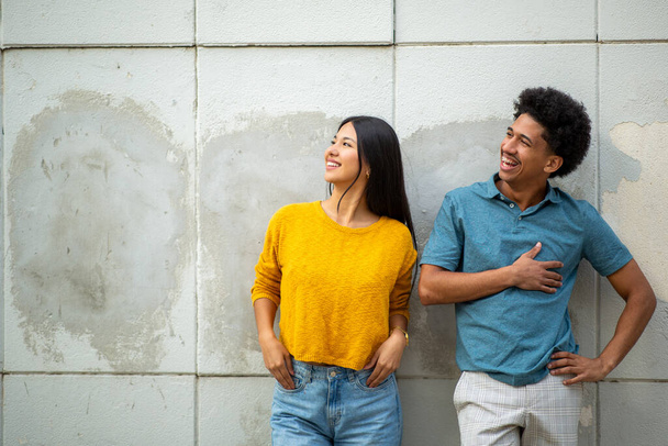 Portrait de jeune couple heureux par mur et détournant les yeux - Photo, image