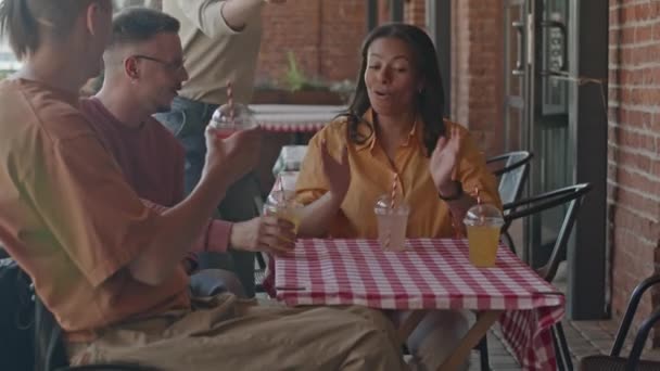 Mittlere Aufnahme von zwei jungen kaukasischen Männern im Rollstuhl und ihren Freundinnen, die zusammen im Sommercafé draußen essen. Eines der Mädchen bringt Pizza in Schachtel auf den Tisch - Filmmaterial, Video