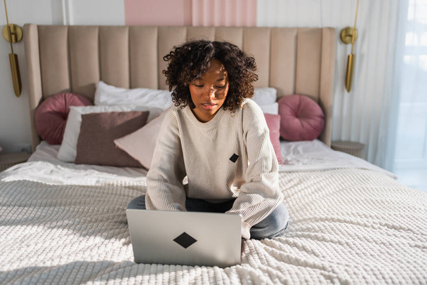 afro-américaine fille à l'aide d'un ordinateur portable dans le lit à la maison bureau dactylographier chat lecture écriture email. Jeune femme noire ayant réunion virtuelle chat en ligne vidéoconférence. Apprentissage du travail à domicile - Photo, image