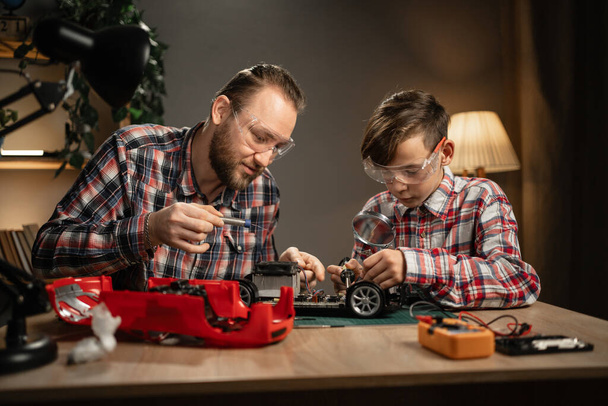 Батько з сином використовує паяльник для ремонту іграшкового автомобіля вдома. Сім'я і вічність. Копіювати простір - Фото, зображення