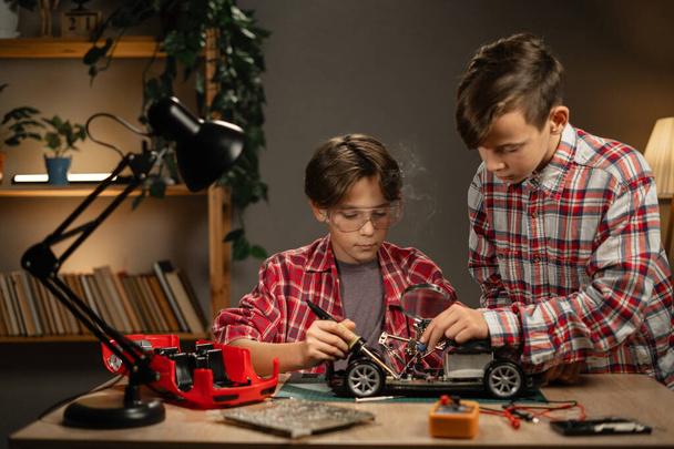 Вечером братья паяльные провода для машины дома. Дети изучают технологии и технологии в мастерской. Копирование пространства - Фото, изображение