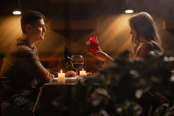 Liebende Frau schenkt aufgeregten Freund beim romantischen Abendessen im Restaurant, Gruß mit Jubiläum, Paarbeziehung. Kopierraum - Foto, Bild