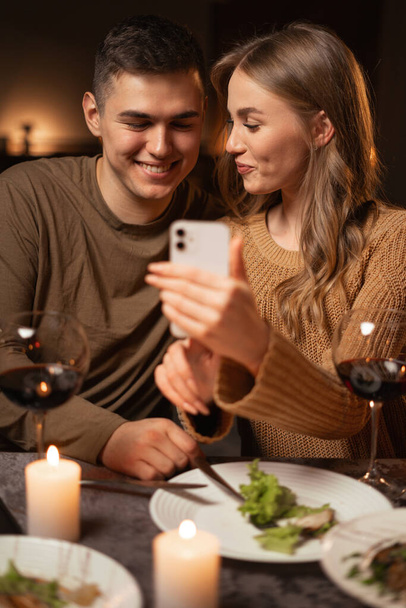 Ευτυχισμένο νεαρό ζευγάρι που χρησιμοποιεί το smartphone περιήγηση στο διαδίκτυο κατά τη διάρκεια ρομαντικό δείπνο ημερομηνία στο σπίτι. Αντιγραφή χώρου - Φωτογραφία, εικόνα