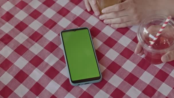 Primer plano del teléfono inteligente con pantalla de la plantilla de croma verde en la mesa de café al aire libre a cuadros - Metraje, vídeo