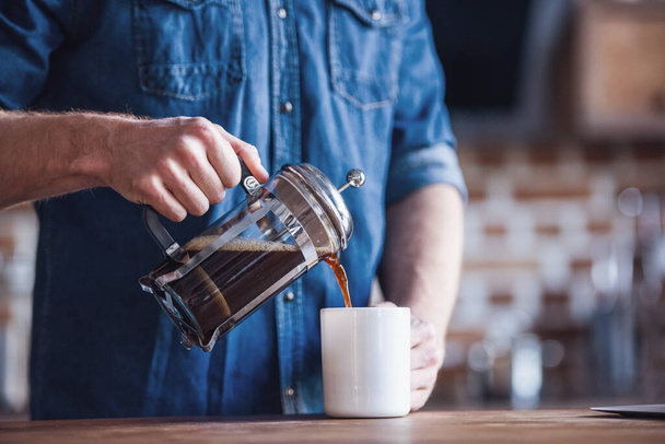 Imagen recortada de un joven que vierte café en la taza mientras está de pie en la cocina
 - Foto, Imagen