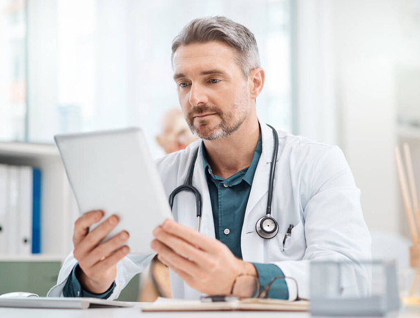 Здоровье и медицинские исследования имеют высокую ценность для общества. зрелый врач, работающий над цифровым планшетом в медицинском кабинете - Фото, изображение
