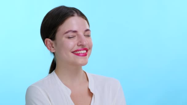 Joyful Caucasian woman laughs heartily against a calming blue backdrop. Laughter is infectious, filling the scene with warmth and happiness. The serene blue background enhances vibrant expression. - Footage, Video