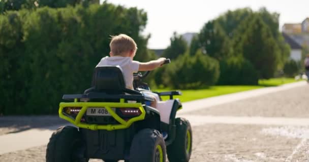 Un bambino che guida un'auto elettrica giocattolo in un parco in una giornata estiva. Un ragazzo guida un quad elettrico. Filmati 4k di alta qualità - Filmati, video