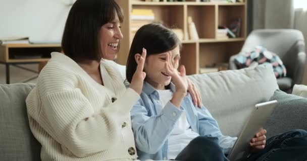 Moeder en zoon gebruiken een digitale tablet voor een videogesprek en zwaaien enthousiast met de handen om iemand aan de andere kant te begroeten. Hun vreugdevolle interactie voegt een gevoel van verbinding en communicatie toe. - Video