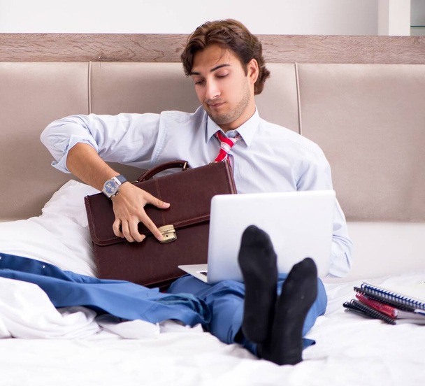 Il giovane impiegato che lavora a casa seduto sul letto - Foto, immagini