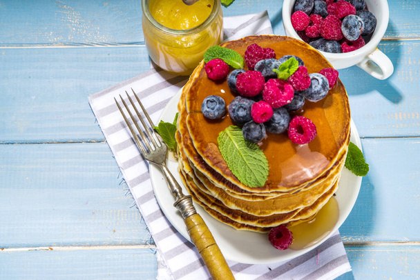 Тарелка вкусных традиционных американских блинчиков со свежими ягодами и сиропом на кухонном столе на светлом фоне - Фото, изображение