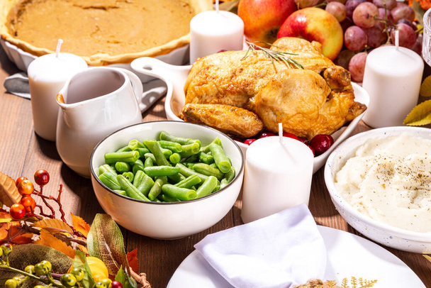 Thanksgiving familie feest tafel dekken met borden, bestek, glazen, traditionele gerechten - gebakken kalkoen of kip, pompoentaart, fruit, aardappelpuree, groene bonen, houten achtergrond - Foto, afbeelding