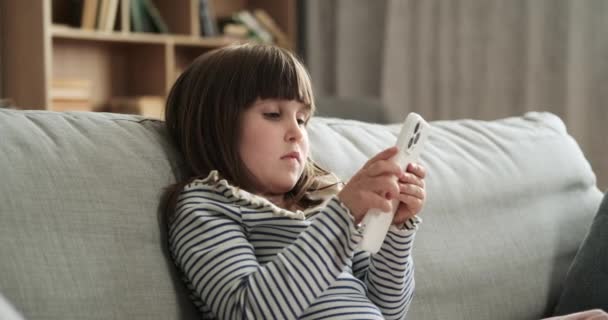 Vakava ajatteleva tyttö istuu sohvalla, syvästi mukana selaamassa puhelinta. Hänen keskittynyt käytöksensä tutkiessaan digitaalista sisältöä lisää mietiskelyä ja keskittymistä tapahtumapaikalle.. - Materiaali, video
