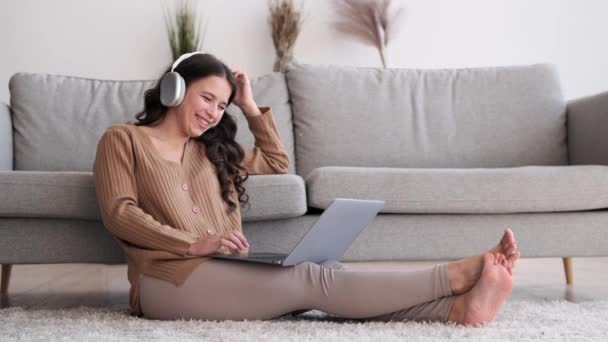 Valkoihoinen nainen yllään kuulokkeet puhkeaa nauruun, kun käytät kannettavaa tietokonetta. Silmät syttyvät huvin vuoksi, ja huone on täynnä tarttuvan naurun ääntä.. - Materiaali, video