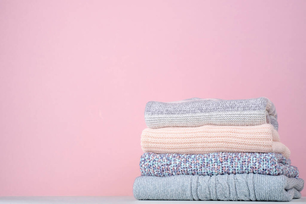 冬のスタックはピンクの背景にセーターを編みました. 季節の変化について。 意識的な消費。 環境の友好的さと持続可能なファッション. テキストのためのスペース。 高品質の写真 - 写真・画像