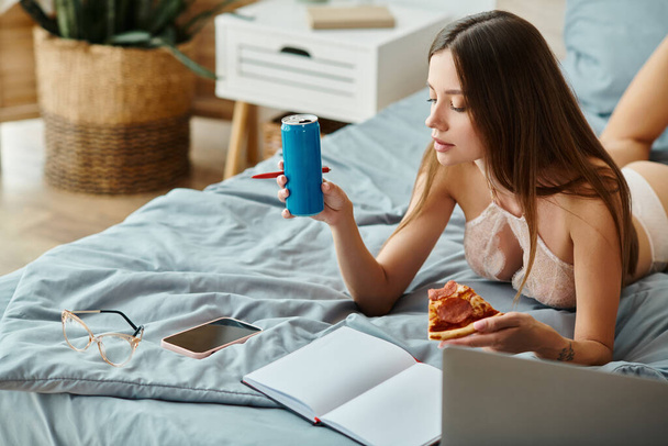 figyelmes fiatal nő szexi fehérnemű feküdt az ágyon pizza és szóda, miközben távolról dolgozik - Fotó, kép