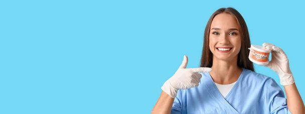 Smiling female dentist holding plastic jaw model on light blue background with space for text - Photo, Image