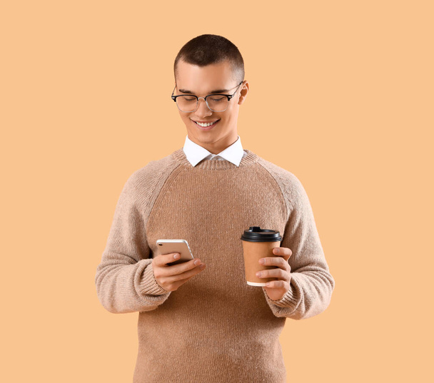 Handsome young businessman with mobile phone and cup of coffee on orange background - Photo, Image