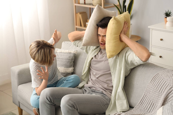 Young man with pillows stressed of his noisy son at home - Photo, Image