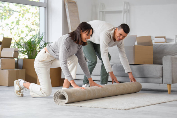 Happy young couple rolling carpet in room on moving day - Photo, Image