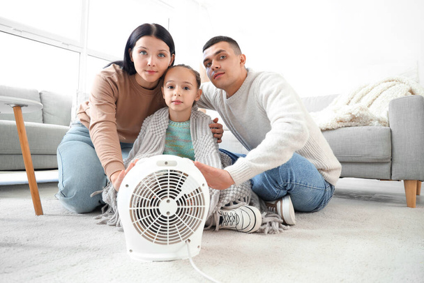 Donmuş aile evdeki elektrikli fan ısıtıcısının yanında ellerini ısıtıyor. - Fotoğraf, Görsel