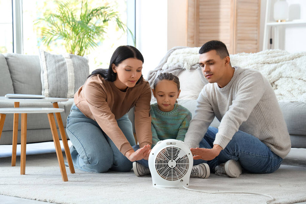Frozen family warming near electric fan heater at home - Photo, Image
